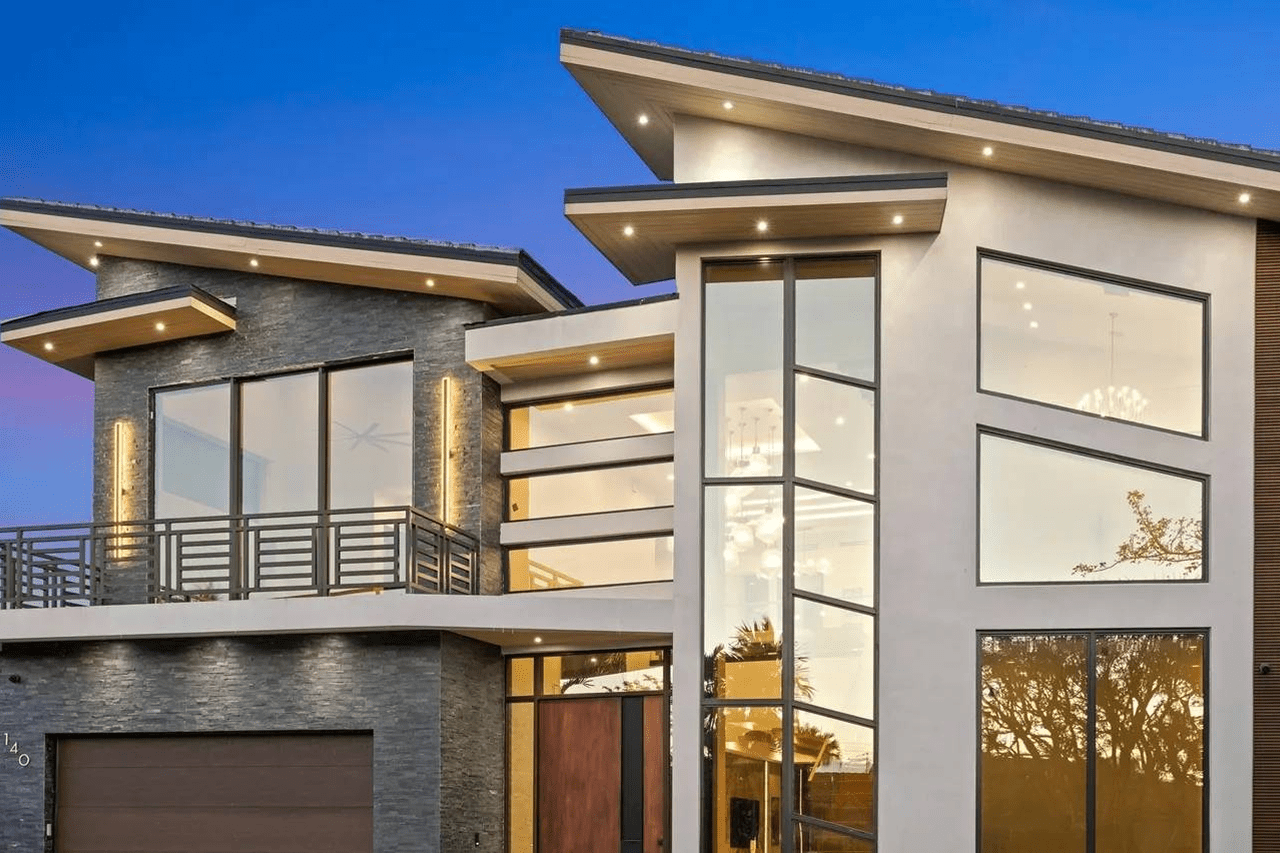 Modern house with large windows and angular roof design at sunset.